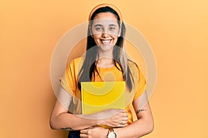 Young hispanic woman wearing student backpack and holding book smiling with a happy and cool smile on face