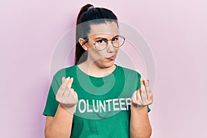 Young hispanic woman wearing volunteer t shirt doing money gesture with hands, asking for salary payment, millionaire business