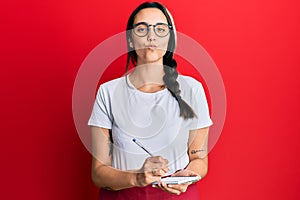 Young hispanic woman wearing waitress apron taking order looking at the camera blowing a kiss being lovely and sexy