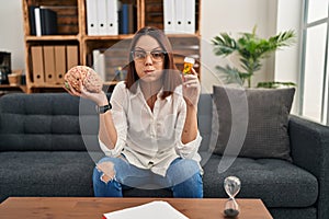 Young hispanic woman working on depression holding pills puffing cheeks with funny face