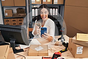 Young hispanic woman working drinking wine and using smartphone celebrating crazy and amazed for success with open eyes screaming