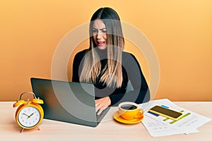 Young hispanic woman working at the office with laptop clueless and confused expression