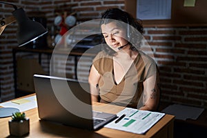 Young hispanic woman working at the office at night looking sleepy and tired, exhausted for fatigue and hangover, lazy eyes in the