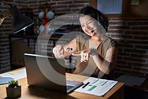 Young hispanic woman working at the office at night pointing to you and the camera with fingers, smiling positive and cheerful