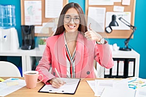 Young hispanic woman working at the office wearing glasses doing happy thumbs up gesture with hand