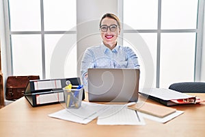 Young hispanic woman working at the office wearing glasses happy face smiling with crossed arms looking at the camera
