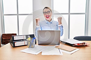 Young hispanic woman working at the office wearing glasses very happy and excited doing winner gesture with arms raised, smiling