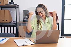 Young hispanic woman working at the office wearing glasses very happy and excited doing winner gesture with arms raised, smiling