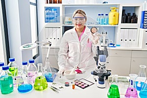 Young hispanic woman working at scientist laboratory doing make up looking positive and happy standing and smiling with a