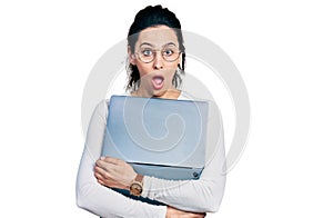 Young hispanic woman working using computer laptop afraid and shocked with surprise and amazed expression, fear and excited face