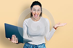 Young hispanic woman working using computer laptop celebrating achievement with happy smile and winner expression with raised hand