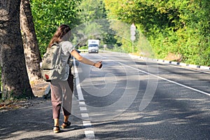 Young hitchhiker with backpack behind her back stops an approaching van with her thumb raised