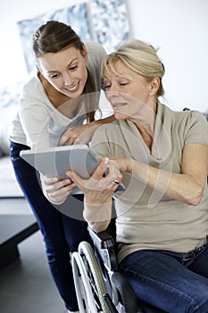 Young home carere with senior lady using tablet