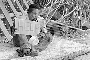 Young homeless African man with cardboard sign asking for help in black and white