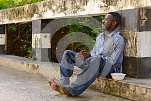 Young homeless African man with plastic bowl looking hungry