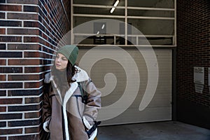 Young homeless girl or woman standing on the street. Evicted female leaning on the building wall, feeling miserable and sad after