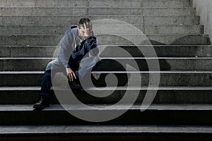 Young homeless man lost job in crisis suffering depression sitting on ground street concrete stairs