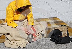 Young homeless man with a yellow hood on a filthy mattress while begging on the sidewalk