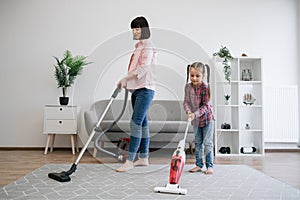 Young homemakers utilizing vacuum cleaners in living room photo