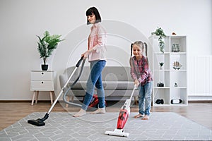 Young homemakers utilizing vacuum cleaners in living room photo