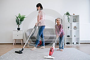 Young homemakers utilizing vacuum cleaners in living room photo
