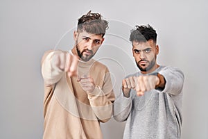 Young homosexual couple standing over white background punching fist to fight, aggressive and angry attack, threat and violence