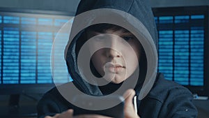 Young hooded hacker kid using a smartphone device to hijack. Genius boy wonder hacks system at cyberspace.