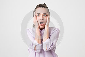 Young horrified woman closing her mouth with hands over white background