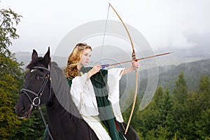 Young horseback girl shooting arrow from bow