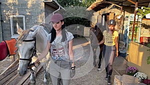 Young horsewomen lead a horses by the bridles to walk.