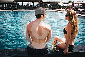 Young hot couple resting at swimpool. Gorgeous sexy man and woman look at each other. Spend time at water in resort spa