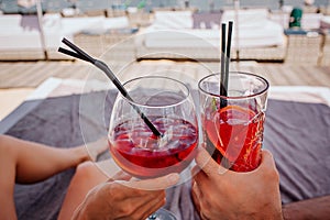 Young hot couple resting at swimpool. Picture of two red cold cocktails with ice cubes cheering. Relax and rest during