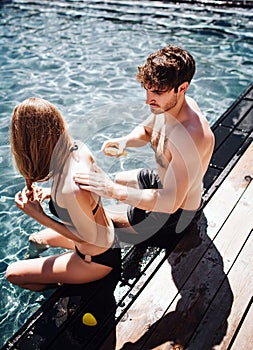 Young hot couple resting at swimpool. Vertical picture of guy put some sun protection cream on girl`s back Take care of