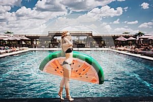 Young hot woman resting at swimpool. Holding ring pool in piece of water melon shape and poses on camera. Stand alone in