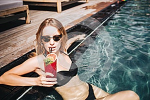 Young hot woman resting at swimpool. Picture of well-built slim and sexy girl drinking red cocktail and enjoy her rest