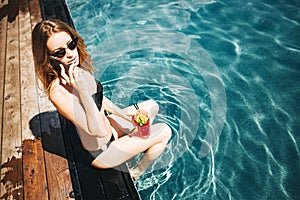 Young hot woman resting at swimpool. Sexy gorgeous girl talking on smartphone during vacation. Woman sit alone at edge