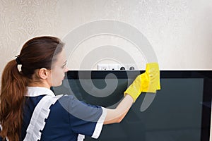 Young housekeeper dusting a television set
