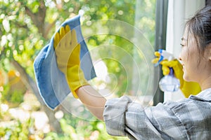 Young housekeeper washing window glass with rag and spray detergent, selective focus. Woman doing professional house cleaning,