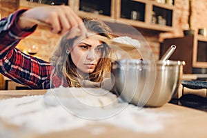 Young housewife in an apron puts flour in a bowl