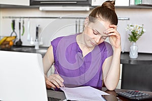 Young housewife calculate family expenses, has to pay bills for rent and gas, looks at papers, works with laptop computer, sits ag