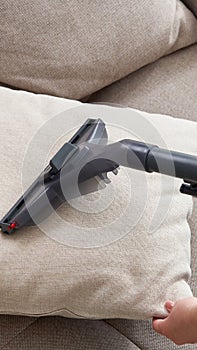 Young housewife Cleaning Sofa with Vacuum Cleaner in living room