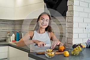 Young housewife cutting  fruits on wooden board while making healthy food for breakfest