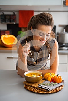 Young housewife eating pumpkin soup in kitchen