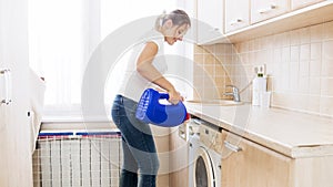 Young housewife pouring liquid detergent in washing machine at laundry