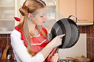 Young housewife in red apron with funny ponytails holds frying p