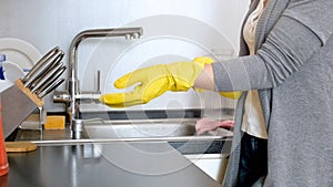 Young housewife standing on kitchen and wearing yellow protective gloves