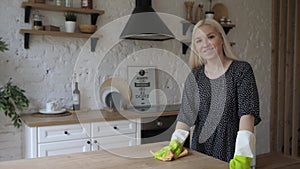 Young housewife wear rubber protective gloves cleans wooden surface and smile 4K
