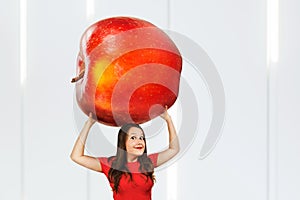 Young hunger pretty funny woman holds huge and large red apple. Girl walks with big heavy fruit