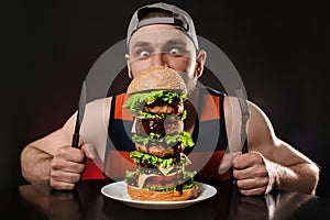 Young hungry man with cutlery eating huge burger on black