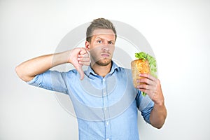 Young hungry man looks hungry holding fresh sandwich with salad leaf showing dislike sign on  white background